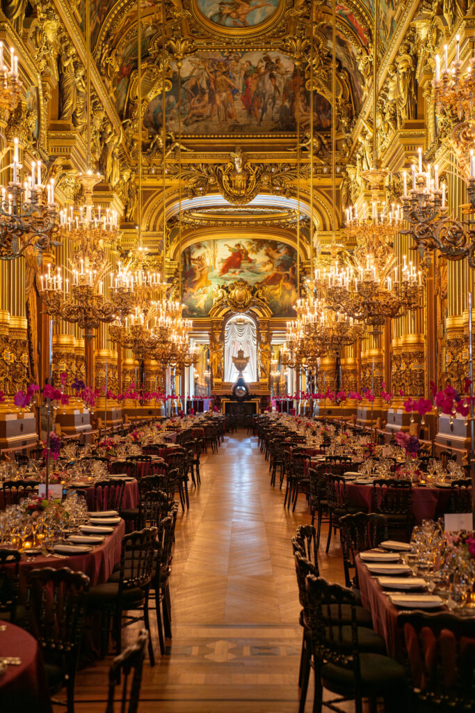 Salle de banquet baroque dorée, lustres abondants et fresques au plafond, tables dressées pour un événement.