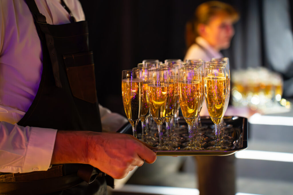 Serveur en tablier noir porte un plateau de flûtes à champagne pleines de bulles.