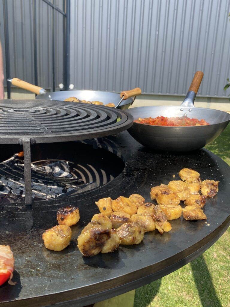 Barbecue extérieur : morceaux de viande dorés sur la grille et poêle de légumes rouges.