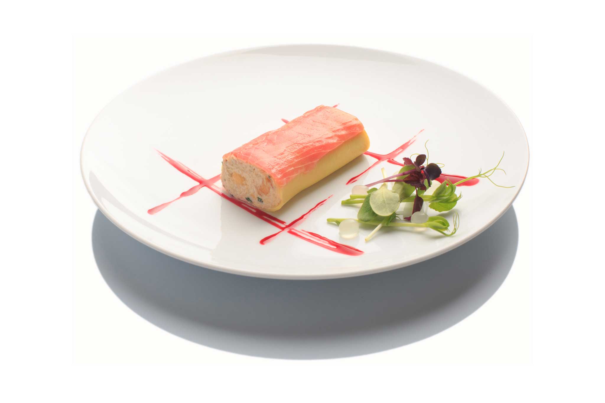 Roulé de saumon rose sur assiette blanche, sauce rouge et micro-pousses.