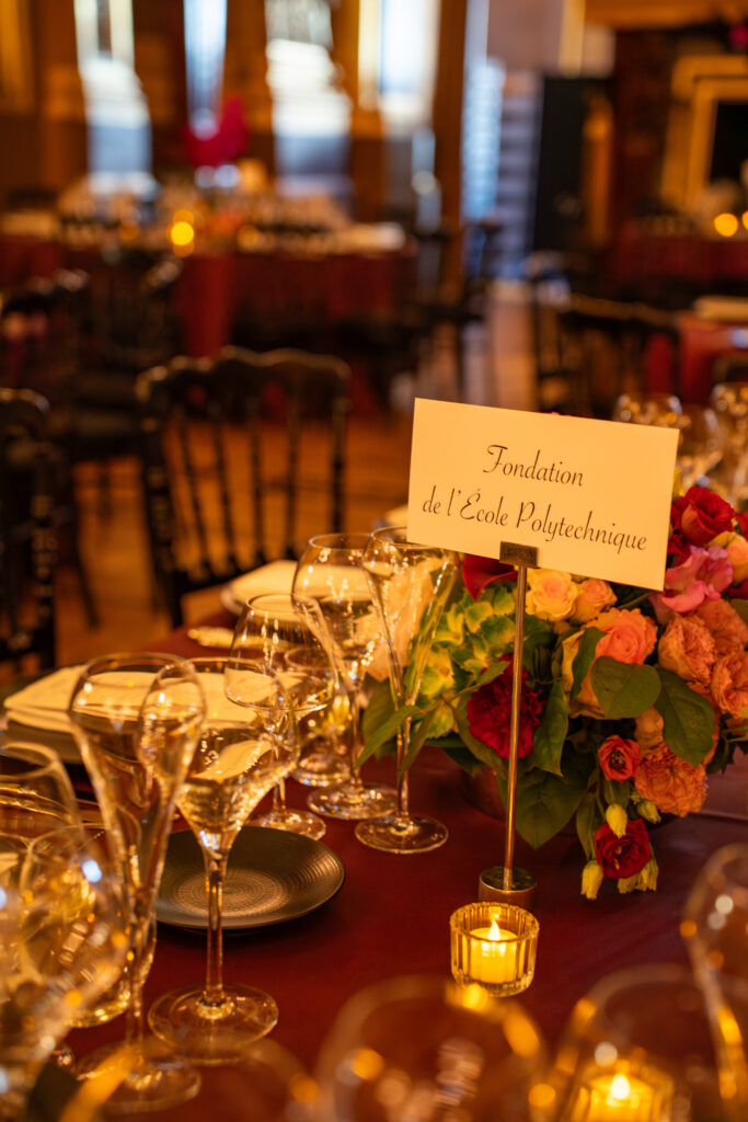 Table de gala décorée de fleurs et bougies avec une carte indiquant Fondation de l'École Polytechnique.