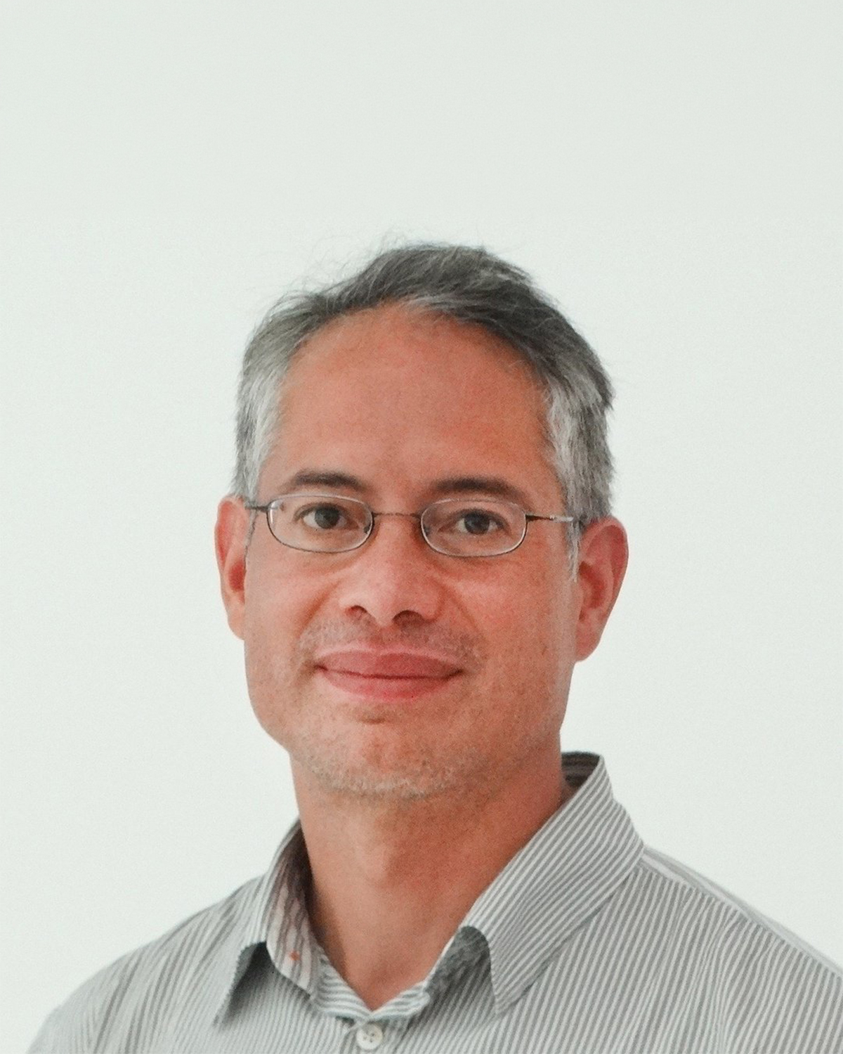 Portrait d'un homme d'âge moyen portant des lunettes et une chemise à rayures, sur fond blanc.