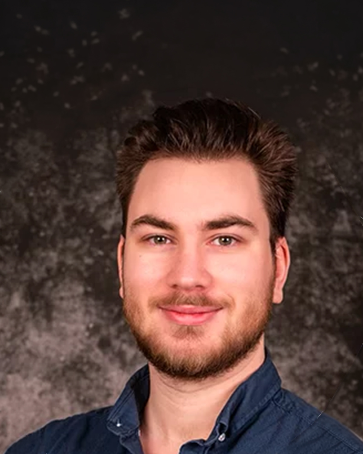Portrait d'un homme jeune, sourire léger, cheveux bruns et barbe légère, chemise bleue.
