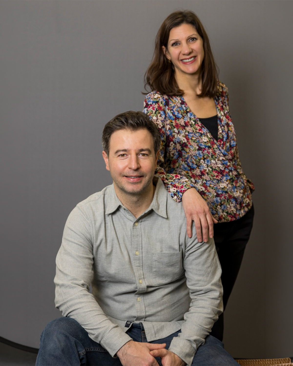 Portrait de deux adultes: un homme assis en chemise gris et une femme debout derrière lui, main sur son épaule, sourire.