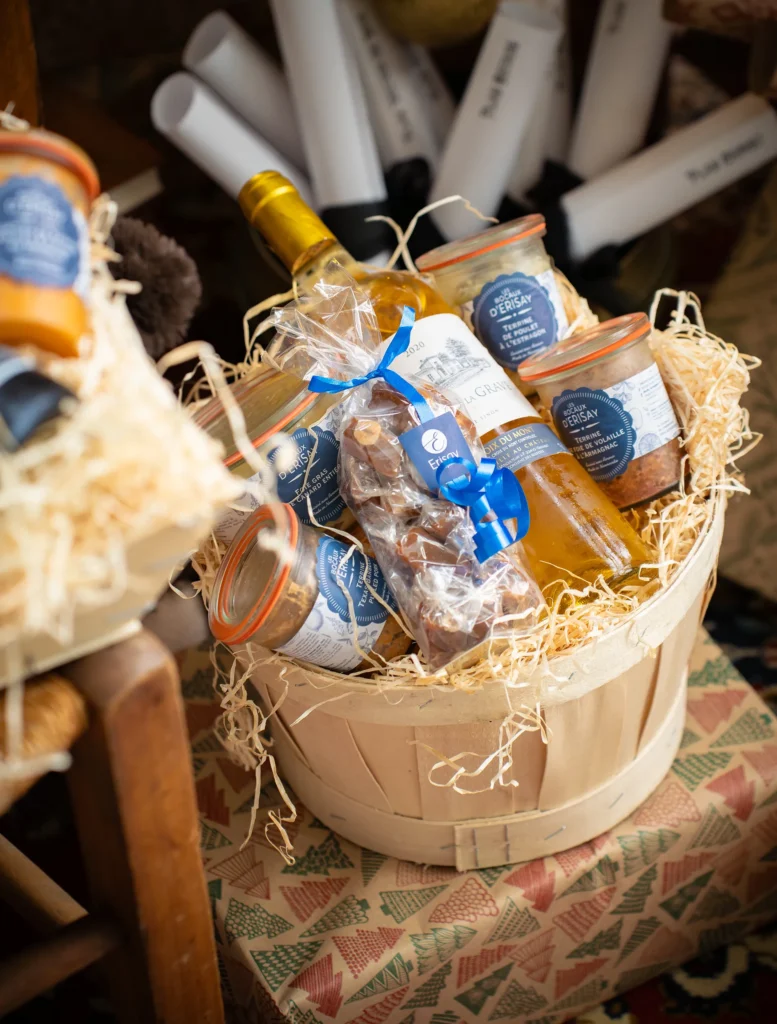Panier cadeau gourmand garni de bocaux et d'une bouteille, étiquettes bleues et rubans.