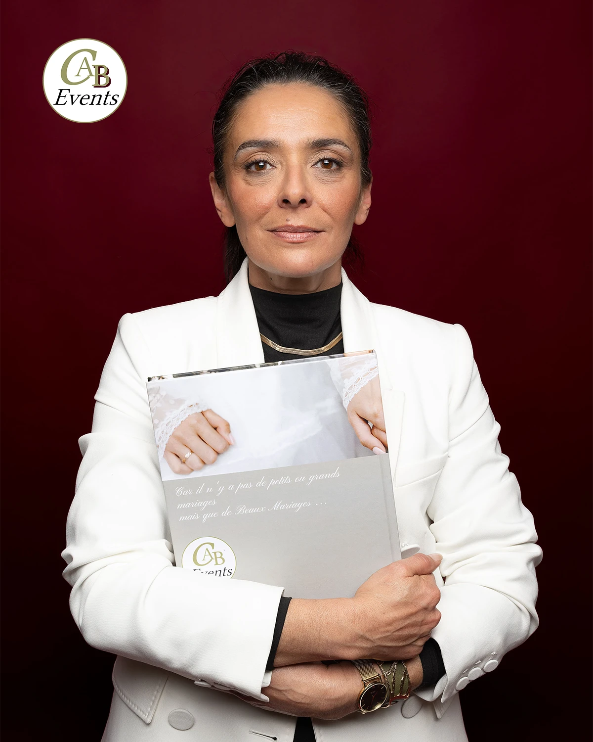 Portrait d'une femme en blazer blanc tenant un livret CAB Events, logo visible, fond rouge.