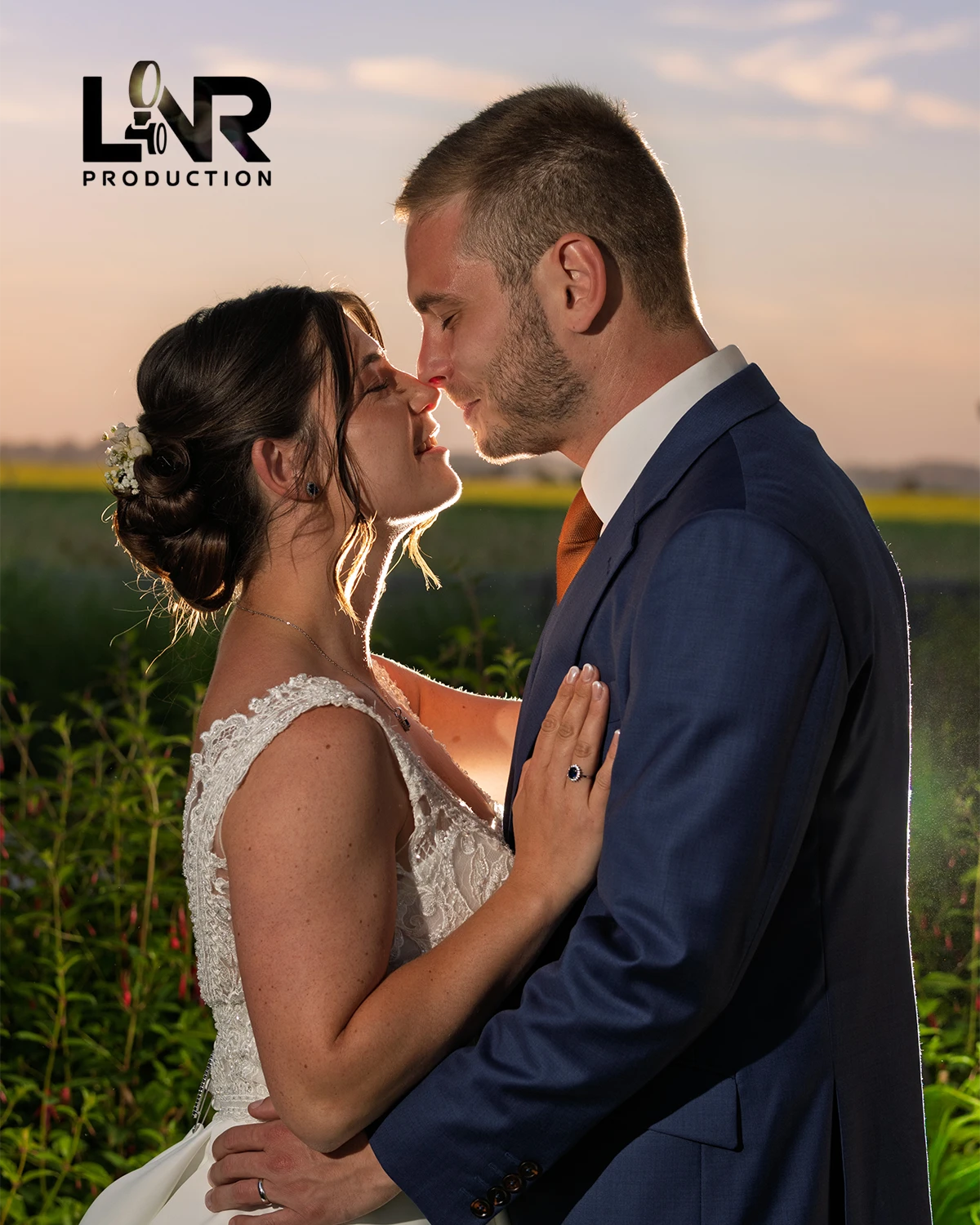 Couple de mariés s'embrassant au coucher du soleil, lui en costume bleu et elle en robe de mariage.