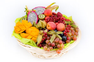 Panier de fruits frais: mangues en cubes, pitaya, kiwis, raisins rouges et noirs, groseilles, framboises et physalis.