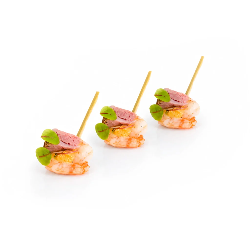 Brochettes de crevettes roses garnies de feuilles de basilic, sauce légère, sur fond blanc.