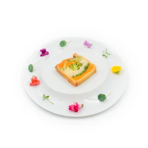 Tranche de pain garnie d'un coulis orange et herbes, décorée de fleurs comestibles sur assiette blanche.