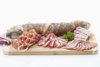 Planche en bois avec baguette et assortiment de charcuterie (jambon tranché et roulé), garnie de persil.