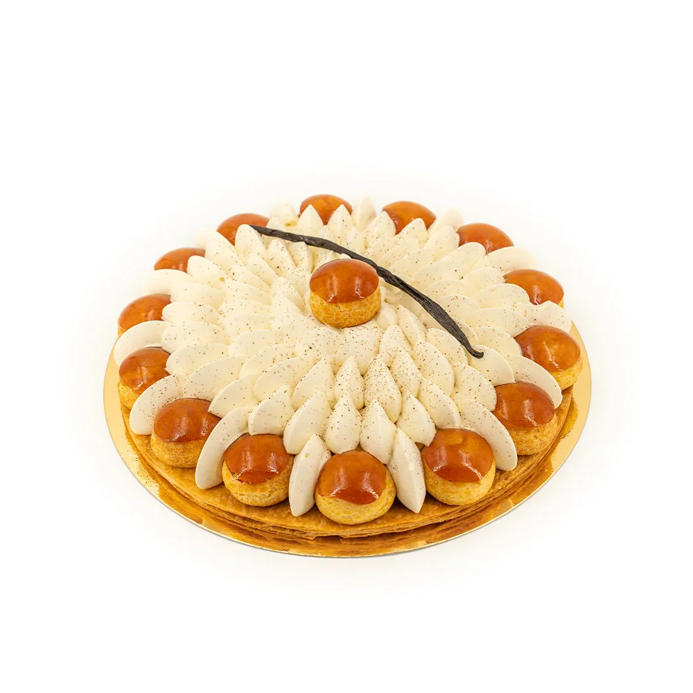Gâteau rond décoré de rosaces de crème blanche et de choux caramelisés autour, vanille au centre.